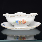 Springer & Co, EPIAG - Checoslováquia(Fundada entre 1918 e 1920 a partir de fábricas nos arredores de Carlsbad). Excepcional molheira em porcelana tcheca da década de 1920. Esmaltagem vítrea na cor branca, formato oblongo, fixada sobre presentoir, com vertedouros opostos revirados para fora, decorada com bela composição botânica em estampagem policromada, predominando as tonalidades amarelo, ocre, azul, coral, verde e marsala, dispostas em agrupamento nas faces do bojo e pequenos ramos distribuídos pela aba do presentoir; orla delimitada por faixa contendo frisos e enrolamentos relevados na própria pasta; borda recortada com contorno ornamentado com aplicação de filete em douradura. Marca da manufatura no verso. Medidas: Alt.: 8 x Comp.: 23 x Larg.: 15 cm. (A Springer & Co de Elbogen na Boêmia foi formada na década de 1880 e encerrou suas atividades em 1945. Ela foi uma das fábricas fundadoras originais da OEPIAG (mais tarde EPIAG), que era uma associação de olarias formadas pelo governo de Viena em 1918 para promover a venda de cerâmica e porcelana da Boêmia. Foi inicialmente denominado OEPIAG, um acrônimo para Österreichische Porzellan Industrie AG ou Austrian Porcelain Industry, mas foi alterado para EPIAG - Erste Böhemische Porzellan Industrie AG que significa Primeira Indústria de Porcelana da Boêmia - em 1920 após a independência da Checoslováquia).