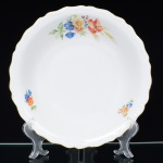 Springer & Co, EPIAG - Checoslováquia(Fundada entre 1918 e 1920 a partir de fábricas nos arredores de Carlsbad). Excepcional bowl em porcelana tcheca da década de 1920. Esmaltagem vítrea na cor branca, formato hemisférico, decorada com bela composição botânica em estampagem policromada, predominando as tonalidades amarelo, ocre, azul, coral, verde e marsala, dispostas em agrupamento lateral e pequenos ramos distribuídos pela aba; orla delimitada por faixa contendo frisos e enrolamentos relevados na própria pasta; borda recortada com contorno ornamentado com aplicação de filete em douradura. Marca da manufatura no verso. Medidas: Alt.: 6 x Diam.: 24,5 cm. (A Springer & Co de Elbogen na Boêmia foi formada na década de 1880 e encerrou suas atividades em 1945. Ela foi uma das fábricas fundadoras originais da OEPIAG (mais tarde EPIAG), que era uma associação de olarias formadas pelo governo de Viena em 1918 para promover a venda de cerâmica e porcelana da Boêmia. Foi inicialmente denominado OEPIAG, um acrônimo para Österreichische Porzellan Industrie AG ou Austrian Porcelain Industry, mas foi alterado para EPIAG - Erste Böhemische Porzellan Industrie AG que significa Primeira Indústria de Porcelana da Boêmia - em 1920 após a independência da Checoslováquia).