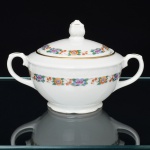 CHODZIEZ PORCELAIN, Chodziez - Polônia(Fundada em 1852 ou 1854, por Hermann Müller e Ludwik Schnorr). Açucareiro em porcelana polonesa da década de 1940; esmaltagem vítrea na cor branca, decorada com faixas contendo padrão floral, aplicado em estampagem policromada, borda delimitada por barrado contínuo relevado na própria pasta, corpo bojudo assentado sobre base circular recortada, tampa ligeiramente abaulada encimada por puxador em forma de flor, alças laterais em voluta com descanso de polegar relevado em folhagem, contornos realçados com filete em douradura. Marca da manufatura no verso. Medidas: Alt.: 10 x Comp.: 16,5 x Larg.: 11,5 cm.