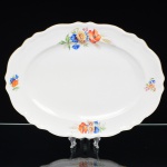 Springer & Co, EPIAG - Checoslováquia(Fundada entre 1918 e 1920 a partir de fábricas nos arredores de Carlsbad). Excepcional travessa oval em porcelana tcheca da década de 1920. Esmaltagem vítrea na cor branca, centro ligeiramente rebaixado, decorada com bela composição botânica em estampagem policromada, predominando as tonalidades amarelo, ocre, azul, coral, verde e marsala, distribuídas pela aba; orla delimitada por faixa contendo frisos e enrolamentos vegetalistas relevados na própria pasta; borda recortada, e ondulada, com contorno ornamentado com aplicação de filete em douradura. Marca da manufatura no verso. Medidas: Comp.: 37,5 x Larg.: 28,5 cm. (A Springer & Co de Elbogen na Boêmia foi formada na década de 1880 e encerrou suas atividades em 1945. Ela foi uma das fábricas fundadoras originais da OEPIAG (mais tarde EPIAG), que era uma associação de olarias formadas pelo governo de Viena em 1918 para promover a venda de cerâmica e porcelana da Boêmia. Foi inicialmente denominado OEPIAG, um acrônimo para Österreichische Porzellan Industrie AG ou Austrian Porcelain Industry, mas foi alterado para EPIAG - Erste Böhemische Porzellan Industrie AG que significa Primeira Indústria de Porcelana da Boêmia - em 1920 após a independência da Checoslováquia).