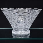 Belíssimo vaso executado em cristal europeu, diáfano e incolor; bojo obcônico ricamente lapidado profundos sulcos, elementos geométricos e estrelas, borda ondulada e recortada, base circular facetada, fundo estrelado. Medidas: