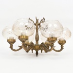 Lustre confeccionado em bronze e metal amarelo, contendo cinco luzes, braços em enrolamento vegetalista com extremo revirado para cima, cúpulas de formato globular achatado em meio cristal incolor, talhadas com motivos geométricos radiais estilizados, organizados com friso contínuo ao redor do bojo. Medidas: Lustre: Alt.:29 x Diam.: 41 cm; Cúpula: Alt.: 11 x Diam.: 14 cm. Apresentes resquício de douramento, necessita ser refeito.