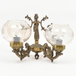 Lustre confeccionado em bronze e metal amarelo, contendo cinco luzes, braços em enrolamento vegetalista com extremo revirado para cima, cúpulas de formato globular achatado em meio cristal incolor, talhadas com motivos geométricos radiais estilizados, organizados com friso contínuo ao redor do bojo. Medidas: Lustre: Alt.: 26 x Diam.: 38 cm; Cúpula: Alt.: 11 x Diam.: 14 cm. Apresentes resquício de douramento, necessita ser refeito.