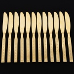 Belíssimo conjunto de facas grandes confeccionadas em metal, dotadas de profusa ornamentação em douradura; lâmina com dorso serilhado, cabo relevado com decoração geométrica repetitiva em recortes simétricos losangulares e formas estilizadas, inseridos em campo texturizado. Fabricação coreana, marca da manufatura no verso. Composto de doze(12)) unidades. Med.: Comp. 21 cm.