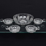 Belíssimo conjunto para sobremesa executado em cristal europeu, diáfano e incolor, ricamente talhado com sulcos, elementos radiais e geométricos, composto de um(01) bowl de formato hemisférico profundo, e quatro(04) taças, de igual formato, com alça lateral circular moldada e aplicada sobre a superfície. Medidas: Alt.: 6,5 x Diam.: 24 cm; Taça: Alt.: 5,5 x Comp.: 14 x Larg.: 11 cm.
