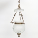 Luminária de teto suspensa em metal com acabamento dourado, composta por estrutura central com braços e elementos de sustentação articulados por correntes.Corpo decorado com motivos fitomórficos em relevo, apresentando aro central ornamentado que sustenta cúpula inferior em vidro opalino, de formato globular, com decoração em relevo de padrão radial. Parte superior com cúpula em vidro fosco, de perfil abaulado, também com motivos geométricos gravados. Sistema de suspensão por correntes metálicas com elos e elementos vazados decorativos. Produção industrial, possivelmente europeia, final do século XIX ou início do século XX. Apresenta pátina no metal, desgaste do douramento, oxidações pontuais e marcas de uso compatíveis com a idade. Medidas: