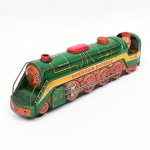 BRINQUEDO ANTIGO. Locomotiva confeccionada em folha-de-flandres litografada, modelo Mountain Express 3430, fabricado pela Modern Toys no Japão durante a década de 1960; mecanismo elétrico a pilhas, representando modelo estilizado de locomotiva a vapor tipo streamlined. Carroceria em metal estampado e litografado, com decoração policromada em verde, vermelho, amarelo e preto, apresentando inscrição MOUNTAIN EXPRESS e numeração 3430. Cabine posterior aberta com figura de maquinista em material plástico moldado. Rodado fixo com rodas estampadas e bielas simuladas em relevo. Base metálica com compartimento para pilhas e motor elétrico, acessível pela parte inferior, com chave seletora de funcionamento. Estado de conservação conforme fotografias, com perdas de policromia, oxidação generalizada na base e componentes metálicos, desgaste por uso e sinais de funcionamento comprometido. Não foi testado, sem, garantias de funcionamento. Medidas: Alt.: 10,5 x Comp.: 40 x Larg.: 8,5 cm.