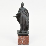 Escultura representando figura feminina executada em metal sobre resina moldada, com acabamento em pátina verdigris simulando bronze. Representa personagem de inspiração clássica, trajando túnica longa e manto drapeado sobre os ombros, com tratamento naturalista das pregas e postura em leve contraposto. Representação iconográfica possivelmente associada a uma das Musas das Artes. Figura assente sobre base quadrangular em mármore, apoiada em plinto. Medidas: 21,5 x Comp.: 8 x Larg.: 5,5 cm. Base: Alt.: 4 x Comp.: 5,5 x Larg.: 5,5 cm. Apresenta sinais de uso e do tempo, pequeno lascado na parte traseira.