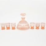 Serviço de licor em vidro soprado, estilo e período Art Déco, composto por uma(01) licoreira com tampa e seis(06) copos, executado em vidro translúcido com gradiente tonal em laranja (amberina/peach tone). O conjunto apresenta decoração por filetes aplicados em esmalte nas tonalidades vermelho e dourado, dispostos em faixas horizontais concêntricas, com leve irregularidade característica de aplicação manual; licoreira possui corpo campaniforme com ombros suaves e gargalo estreito, rematado por rolha lapidada, copos seguem tipologia obcônica com base anelar destacada. Medidas: Licoreira: Alt.: 15 x Diam.: 13 cm; Copos: Alt.: 6 x Diam.: 4,5 cm. Apresenta desgaste no esmalte e douradura.