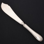Mappin & Webb, Mappin & Webb, Londres - Inglaterra(Fundada em 1775). Elegante espátula para serviço de peixe confeccionada em metal espessurado à prata, fabricação inglesa; lâmina com dorso recortado e ondulado, cabo de ponta oval, relevado com frisos, fitas, volutas e folhagens. Marca da manufatura na lâmina. Medida: