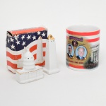 Três(03) itens de coleção: a) Saleiro e pimenteiro modelados em forma de marcos arquitetônicos dos Estados Unidos: edifício do Capitólio (inscrição U.S. Capitol) e obelisco do Washington Monument. Superfícies em esmalte branco com aplicações pontuais de douração. Perfurações superiores para saída de sal e pimenta. Acondicionados em caixa de papelão com decoração alusiva à bandeira dos Estados Unidos. Medidas:  b) Caneca cilíndrica com alça lateral em porcelana com impressão por decalque policromado, representando a cerimônia de posse presidencial dos Estados Unidos, com efígies de Barack Obama e Joseph Biden, inscrição Inauguration January 20th 2009, bandeira estadunidense e imagem do Capitólio. Borda superior com faixa vermelha. Medidas: