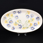 Travessa oval em cerâmica, esmaltação de tom marfim, borda lisa levemente elevada, decorada com composição floral policromada aplicada por pintura manual, distribuída pela superfície interna. Medidas: