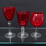Três taças em vidro rubi, bojo liso, bases circulares em vidro incolor, hastes distintas, sendo uma com haste lisa, uma torcida e outra curta. Vidro sobreposto, coloração obtida por camada externa rubi sobre base incolor. Medidas: