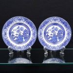 English Ironstone Tableware, Staffordshire, Inglaterra. Dois(02) pratos rasos em faiança inglesa, esmaltagem branca, centro dotado de rica decoração com o clássico padrão "Willow", retratando paisagem fluvial com ponte, pássaros, embarcação e pagode, borda circundada com padrão floral e geométrico contínuo. Marca da manufatura no verso. Medida: Diam.: