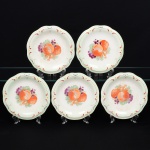 Conjunto de seis(06) pratos para pão, ou doce, em faiança, de formato circular com aba levemente recortada em ondulações suaves e cavidade central côncava. Decoração central representando composição de frutas(pêssegos, uvas e bagas) dispostas sobre folhagem, executada por transferência e pintura complementar. Aba ornada por filetes curvos em esmalte vermelho, intercalados por pequenos elementos geométricos em amarelo e traços pontilhados em preto, compondo motivo estilizado. Marca da manufatura no verso. Um com acentuada quebradura no verso da borda, um com pequeno bicado, todos com leves manchas do tempo e marcas de uso. Medida: Diam.: 19 cm.