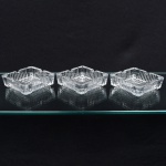 Conjunto de três(03) cinzeiros em cristal moldado, translúcido e incolor; formato quadrangular com bordas recortadas e cavidades nos vértices para apoio do cigarro, paredes com relevo vertical repetitivo e base espessa. Medidas: