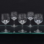 Conjunto de taças em cristal francês, diáfano e incolor, para vinho tinto; bojo lavrado com faixa torcida suspendendo guirlanda de flores e laçarotes, fuste cilíndrico sobre base circular. Composto de cinco(05) unidades. Medidas: Alt.: 13,5 x Diam.: 5 cm.