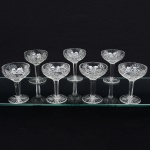 Conjunto de taças de pé alto em cristal europeu, diáfano e incolor, para champanhe; bojo hemisférico dotado de profunda lapidação, contendo padrão de estrelas, sulcos, losangos e palmetas, haste sextavada, topo circundado por fileira de janelas ovais, apoiada sobre base circular, fundo preenchido por estrela raiada de dezesseis pontas. Composto de sete(07) unidades. Medidas: Alt.: 12 x Diam.: 9 cm.
