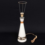 Base de abajur em cerâmica esmaltada com elementos em metal; corpo em formato cônico alongado com base circular, esmaltação branca com faixa decorativa aplicada na porção inferior com representação de animais em paisagem, anel intermediário em acabamento metálico, soquete superior com suporte metálico para fixação de cúpula e instalação elétrica aparente; Estado conforme fotografias. Medidas: