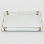 Bandeja retangular espelhada, base em placa plana com bordas lapidadas, apoiada sobre quatro pés metálicos circulares. Estrutura superior composta por galerias laterais formadas por hastes tubulares paralelas em vidro, fixadas por suportes metálicos nos cantos, em metal dourado. Montagem por elementos metálicos rosqueados, visíveis na face inferior. Medidas: