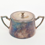 Açucareiro com tampa em metal prateado, de corpo aproximadamente cônico, com bordo superior reentrante para encaixe da tampa. Apresenta duas alças laterais simétricas, vazadas, de seção angular, aplicadas junto à borda. Tampa circular com pega central em formato de botão. Marca da manufatura no verso. Necessita polimento, apresenta desgastes no banho de prata. Medidas: Alt.: x Comp.: x Larg.: