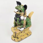 Escultura em cerâmica esmaltada representando leão guardião chinês (Shishi / Fo Dog), modelado em vulto pleno, em posição sentada sobre base integrada. Figura de caráter apotropaico, com cabeça de feições expressivas, boca aberta exibindo língua projetada e presas, olhos salientes aplicados e orelhas eretas. Corpo robusto com dorso ornado por estilização da juba em elementos globulares e crista dorsal em relevo. Peitoral decorado com colar em forma de contas, típico da iconografia desses guardiões. Superfície recoberta por esmaltação policroma em verde, amarelo, azul e branco, com acentuado craquelê (craquelure) e áreas de desgaste que expõem a pasta cerâmica. Base de contorno irregular, igualmente esmaltada, com decoração abstrata. Escultura ornamental, inspirada na tradição sino-oriental de esculturas protetoras de templos e residências, reinterpretada em produção posterior.Estado de conservação conforme fotografias: apresenta perdas de esmalte, fissuras, restauros antigos e lascas, notadamente nas orelhas, dentes e extremidades. Medidas: Alt.: x Comp.: x Larg.: