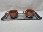 Lote de 2 canecas de consume em porcelana e bandeja retangular em aço inox. Medindo a bandeja 46cm x 16cm.