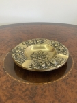 Cinzeiro em bronze, formato circular, diâmetro 13cm. Borda decorada em relevo com motivos florais em sequência e quatro apoios para cigarro. Centro igualmente ornado com flor em relevo. Apresenta pátina natural e sinais compatíveis com o tempo.
