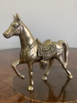 Escultura representando cavalo em bronze, com sela e arreios ricamente ornamentados em relevo. Figura em posição altiva, com uma das patas dianteiras elevada. Altura 16,5cm e comprimento 15cm. Apresenta pátina natural e sinais compatíveis com o tempo.