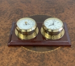 Conjunto alemão composto por barômetro e relógio em metal dourado, fixados sobre base com moldura em madeira. Mostradores com numeração romana e indicação meteorológica. Medidas totais: 22x12cm