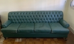 Sofá em couro na cor verde com encosto em capitonê e braços arredondados. Assento composto por almofadas soltas e pés em madeira. Medidas: 223cm de largura, 78cm de profundidade e 82cm de altura. Apresenta desgastes naturais do tempo e uso no revestimento.