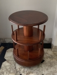 Mesa auxiliar circular em madeira própria para apoio de livros em uso. Apresenta três níveis e base com rodízios. Estrutura central cilíndrica e hastes verticais de apoio, faltando uma das hastes em madeira. Altura: 78cm. Diâmetro: 53cm. Apresenta marcas compatíveis com o uso e o tempo.