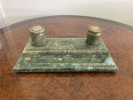 Tinteiro de mesa em pedra alabastro italiana, com dois reservatórios e tampas decoradas com moedas metálicas aplicadas. Apresenta um dos reservatórios com a tampa e a moeda desprendidas. Largura 30cm.