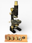 INSTRUMENTO ÓPTICO, um (1) microscópio antigo, corpo em metal com acabamento preto e detalhes em latão, com inscrição Nachet  Paris, com ajustes laterais e mesa circular. Acompanha base/suporte em madeira com jogo de objetivas/lentes avulsas (diversas unidades), acondicionada em caixa original, apresenta sinais de oxidação, vendida no estado da foto, medindo 30cm de altura.