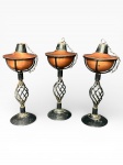 DIVERSOS, três (3) lamparinas confeccionadas em ferro fundido com esmaltagem preta, corpo com moldagem geométrica em vazados, recipiente para querosene em metal cobreado com abafadores, medindo 29cm de altura.