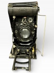 FOTOGRAFIA, uma (1) câmera fotográfica antiga de fole (tipo dobrável), marca Nixe, equipada com lente Zeiss Ikon e obturador Compur, com estrutura metálica, trilhos frontais e suporte/haste lateral, vendida no estado, possui quebra na esteira.