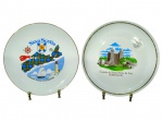 PORCELANAS, dois (2) pratos decorativos souvenir confeccionados em porcelana branca, sendo: A) um (1) prato Nova Scotia, Canadá, com mapa ilustrado, símbolos náuticos e inscrição Canadas Ocean Playground, medindo 24cm e B) um (1) prato Castelo de Santa Maria da Feira  Portugal, com ilustração do castelo e filetes na borda, medindo 25cm, falhas na douração.