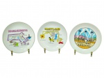 PORCELANAS, conjunto com três (3) pratos decorativos temáticos (EUA) confeccionados em porcelana branca, sendo: A) um (1) prato MASSACHUSETTS, com mapa ilustrado e nomes de cidades; B) um (1) prato MARYLAND  The Old Line State, com mapa ilustrado e inscrições; C) um (1) prato HOLLYWOOD  CALIFORNIA, com cena temática em policromia, medindo 18,5cm.