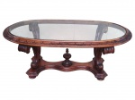 MOBILIARIO, uma (1) mesa de centro confeccionada em madeira entalhada a mão, tampo oval em vidro com guarnição entalhada em folhagens, sustentado por quatro pés finalizados em volutas, apoiadas sobre base recortada com bilro na parte central, medindo 44x119x63cm.