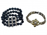 BIJUTERIAS, duas (2) peças, sendo: A) 1 bracelete elásticode 3 voltas com contas em cristal facetado na tonalidade preta e barretes metálicas com incrustações de zircônia e B) 1 pulseira em metal dourado decorado por flor com incrustação de pedrarias sintéticas com falhas na douração, medindo 19cm de comprimento.