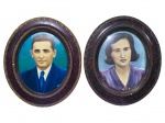QUADROS, dois (2) quadros ovais, com retratos masculino e feminino, em imagem colorizada/pintada (tipo foto pintada / reprodução artística), com fundo em tons azulados. Peças emolduradas em molduras ovais de acabamento escuro, com frisos e ornamentos em tom dourado, apresentando falhas na patina e 1 possui vidro convexo quebrado, medindo 42x36cm, 1 possui sinais de cupim tratado.