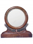 ESPELHO, um (1) espelho de mesa redondo com base confeccionada em madeira escura, decorado por folhagens relevadas e entalhes de frisos em baixo relevo, medindo 29,5x28,5cm.
