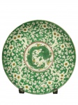 PORCELANA ORIENTAL, um (1) prato decorativo confeccionado em porcelana oriental, de formato circular, com decoração esmaltada em tons de verde, branco, amarelo e detalhes em vermelho, apresentando ao centro dragão estilizado, ladeado por motivos florais e vegetalistas em toda a aba; verso com marca apócrifa em azul sob o vidrado e elementos florais ao redor, medindo 22cm.