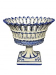 FAIANÇA, uma (1) fruteira confeccionada em faiança vitrificada com manufatura ilegível, decoração vazada e elementos vegetalistas na tonalidade azul e borda dentada, medindo 17,5x19,5cm.