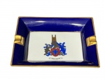 NEOCLASSICA (Portugal), um (1) cinzeiro confeccionado em porcelana portuguesa na tonalidade branca, borda na tonalidade azul cobalto com filetes em ouro, centro com brasão heráldico policromado com inscrição Honra e Bravura, medindo 18,5x15cm.