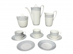 PORCELANA STEATITA, parte de serviço para café com seis (6) peças, sendo: A) 1 bule para café, medindo 19x18,5x8,5cm, B) 1 açucareiro, medindo 11x9,5x9,5cm, C) 1 leiteira, medindo 13x13x7,5cm e D) 3 xícaras para café com seus respectivos pires, medindo 5x7,5x6cm, confeccionadas em porcelana branca com espessa faixa azul com guirlanda floral em tom fosco e filetes em prata.