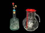 VIDROS, lote com duas (2) peças, sendo: A) 1 licoreira confeccionada em vidro translucido com moldagem floral e tampa metálica representando Galo de Barcelos esmaltado em policromia, medindo 28,5cm e B) 1 jarra italiana confeccionada em vidro translucido, corpo bojudo, tampa com recipiente para gelo e acompanha mexedor, medindo 22cm de altura.