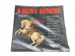 DISCO DE VINIL, um (1) disco de vinil LP, intitulado O Valente Guerreiro, selo Tropicana, em capa original ilustrada, trazendo repertório de cânticos e pontos ligados à Umbanda, com faixas como Filho de Umbanda, Proteção de Xangô, Rainha do Mar, Guia de Iemanjá e Santo Guerreiro, não testado e sem garantia de funcionamento.