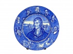 ROYAL DOULTON (A empresa foi fundada em 1815, em Lambeth, Londres, por John Doulton, junto com Martha Jones e John Watts), um (1) prato decorativo confeccionado em faiança inglesa na tonalidade branca, representando Robert Burns, cercado por cenas e títulos de suas obras famosas ao fundo na tonalidade azul, medindo 25,5cm de diâmetro.