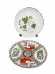 PORCELANAS, dois (2) pratos decorativos confeccionados em porcelana na tonalidade branca, sendo: A) 1 decorado por cachos de uva e folhas de parreira em policromia com borda filetada na cor verde, medindo 18,5cm e B) 1 ricamente decorada por elementos florais, vegetalistas e figuras orientais em policromia ao gosto Familia Rosa com realces em ouro, medindo 19cm.